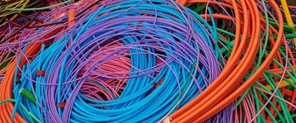 Färgglada återvunna plastkablar i blått, orange, rosa, lila och grönt, sammanflätade i en hög. Elektroniskt avfall och återvinningsmaterial.