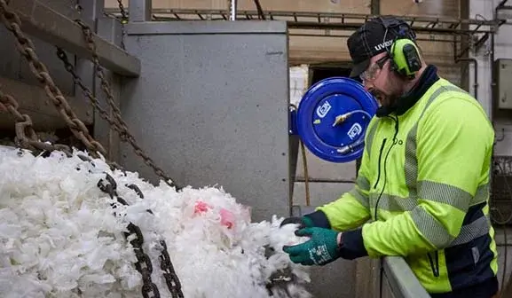 Man i varselkläder hanterar plastflingor i återvinningen
