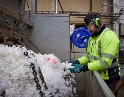 Plastflingor i maskin för återvinning. Man i varselkläder står intill och ser till så att det matas i korrekt.