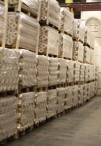 Stora rullar av plastfilm i lagerlokal. Materialinformation om plast och dess olika användningsområden.